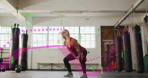 Woman athlete squatting with kettlebell in boxing gym with augmented fitness data overlay