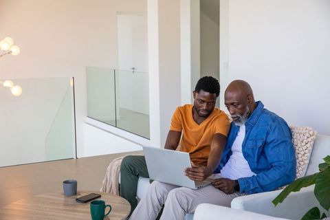 Father and adult son using laptop together in modern living room
