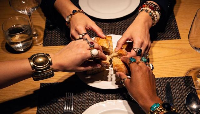 Breaking bread together wearing bold rings and stacked bracelets closeup on hands