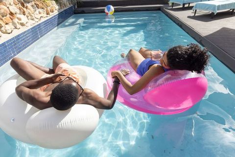 Sunlit interracial couple floating and holding hands on pool rings in backyard summer