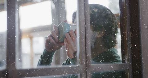 Man Enjoys Coffee Indoors While Snow Falls Outside During Christmas