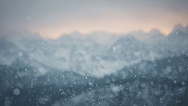 Drifting snow over hazy alpine ridgelines at dawn with soft bokeh horizon glow