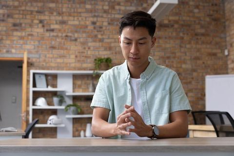 Asian man sitting in modern office meeting space contemplating safety