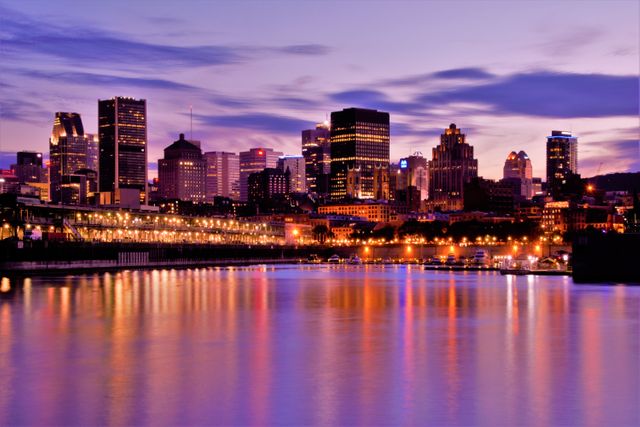 Cityscape showing downtown high-rise buildings reflected in a calm river during sunset. Twilight sky filled with purple and blue hues and city lights illuminating the scene. Suitable for use in travel brochures, tourism advertisements, urban living articles, and real estate promotions highlighting the beauty of city life.