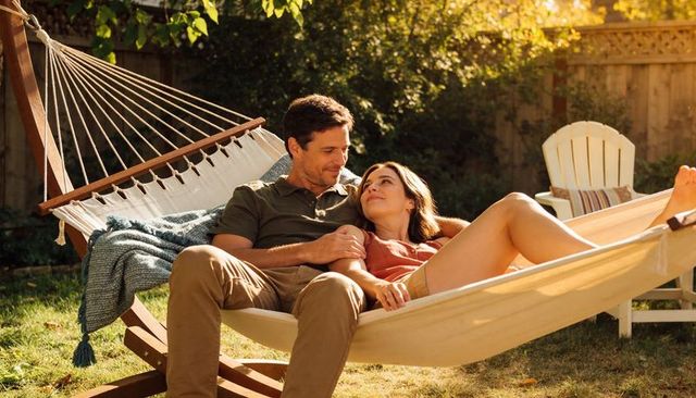 Couple relaxing in hammock on sunny backyard with knit blanket and adirondack chair