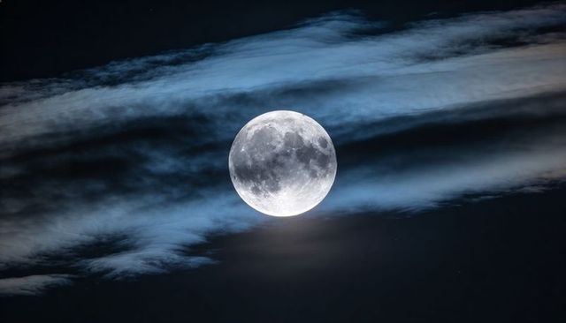 Full moon glowing through thin cirrus clouds in deep blue night sky