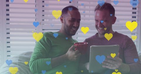 Diverse Gay Couple Smiling with Tablet and Heart Overlays