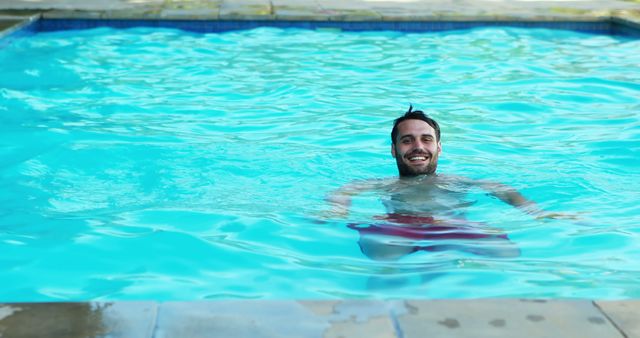 A man is smiling while relaxing in an outdoor swimming pool on a sunny day. This image is perfect for promoting summer activities, leisure, vacation resorts, and healthy lifestyles. It can be used in advertisements, travel brochures, magazines, and websites related to swimming, holiday destinations, or relaxation.