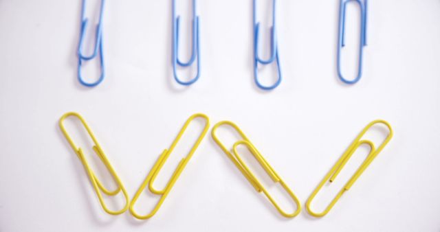 Blue and yellow paper clips arranged sporadically on a white background. Represents school or office supplies, organization, minimalistic design, and color contrast. Use for marketing materials, stationery branding, educational resources, or organizational blog posts.