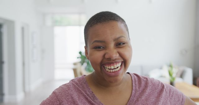 Portrait of smiling african american plus size woman looking at camera and laughing in living room. domestic lifestyle, enjoying leisure time at home.