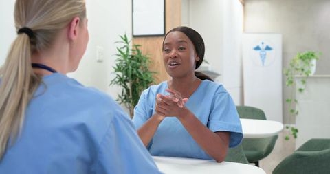 Diverse nurses collaborating in clinic breakroom, discussing patient care and teamwork
