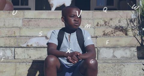 Pensive boy sitting on sunlit stone steps wearing backpack with dogs and floating letters