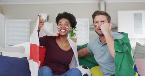 Interracial couple enjoying football game at home with national flags