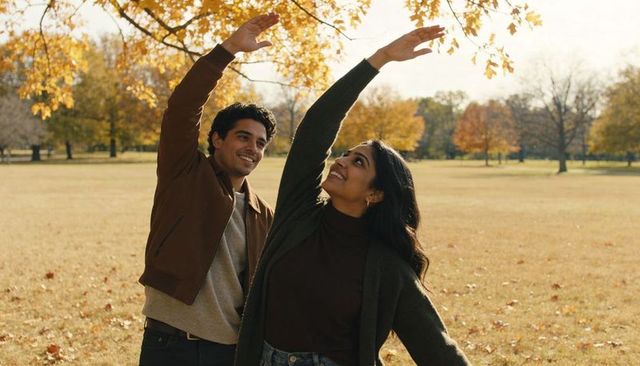 Young couple reaching for golden autumn leaves in park during golden hour sunlight