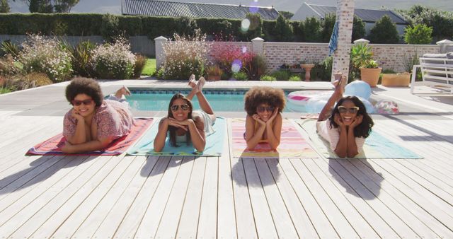 Group of diverse friends lying on colorful towels by pool on sunny day, wearing sunglasses, smiling. Captures moment of pure joy and leisure, making it perfect for promotions about summer holidays, relaxation retreats, poolside events, and friendly gatherings. Ideal for travel brochures, social media ads, and lifestyle blogs.