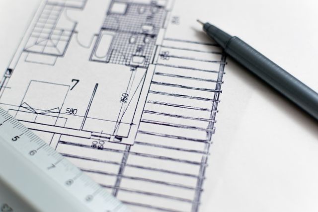 Shows architectural blueprint on desk with pen and metal ruler. Useful for topics related to architecture, engineering, design projects, construction planning, and drafting instrutions. Ideal for illustrating planning stages, design processes, and the importance of precision and detail in architectural work.