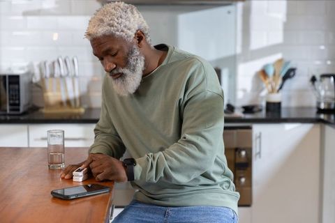Senior african american man checking pulse oximeter at kitchen counter