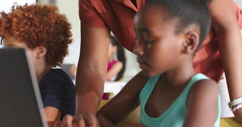 African American teacher guiding student using laptop for collaborative classroom learning