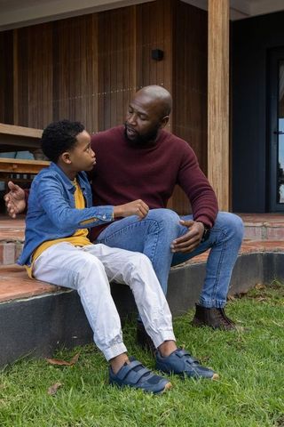 African american father coaching son on porch steps showing warmth, bonding, and parenting