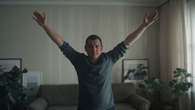 Man raising arms in serene living room with sofa and houseplants soft natural light