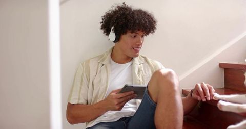 Young man relaxing on home stairs listening to music with tablet and friend nearby