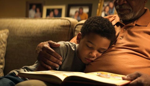 Grandfather cradling grandson reading bedtime story on cozy living room sofa
