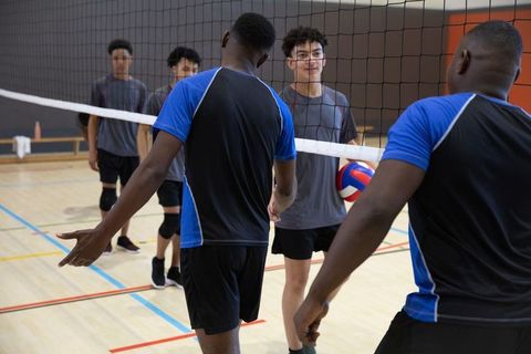 Teenage volleyball players shaking hands at net showing sportsmanship and team unity