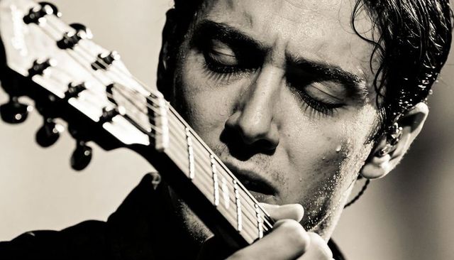 Sweaty male guitarist playing intense closeup pressing strings on neck under spotlight