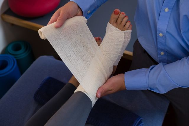 Medical professional wrapping bandage around injured foot of patient in clinical setting. Ideal for depicting healthcare services, physical therapy, rehabilitation methods, and patient care. Useful for medical websites, health magazines, and educational materials.