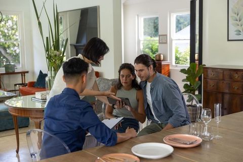 Young couple receiving home consultation at dining table while advisor showing tablet