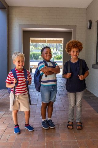 Multiracial elementary school boys standing together wearing backpacks on brick porch