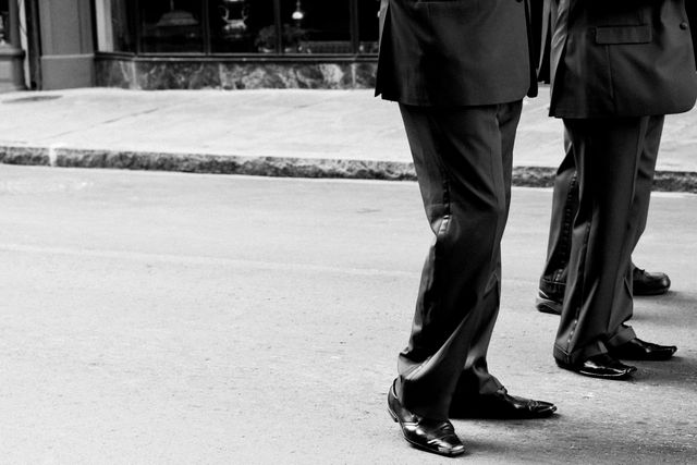 This image depicts two businessmen walking together on a city street, both wearing formal attire. The perspective focuses on their lower bodies, highlighting their polished shoes and the urban environment. This can be useful for illustrating partnership, professionalism, urban life, and business settings in marketing materials or articles related to business, fashion, or urban commuting.