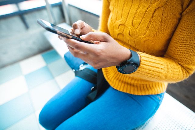 Midsection of African American businesswoman using smartphone while sitting at airport. Ideal for content related to travel, business, technology, and modern communication. Can be used in articles, blogs, and advertisements focusing on connectivity, digital tools, and transportation.