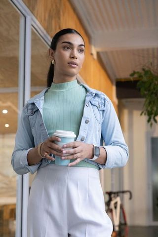 Young woman holding takeaway coffee in urban lobby wearing denim jacket and smartwatch