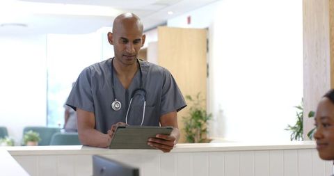 African american doctor reviewing tablet at bright clinic reception with stethoscope