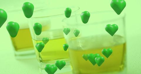 Floating emerald hearts over square glass tumblers holding amber liquid, surreal still life