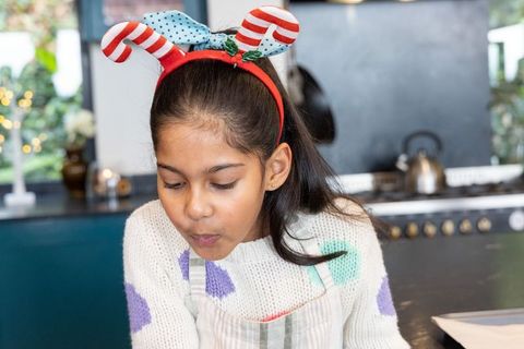 Indian preteen wearing festive reindeer headband cooling baked treats on kitchen counter