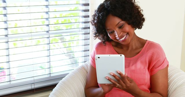 A smiling African American woman sits comfortably while browsing on her tablet, with copy space - Download Free Stock Photos Pikwizard.com