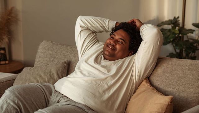 Relaxing man lounging on beige sofa in cozy living room wearing white top and gray pants