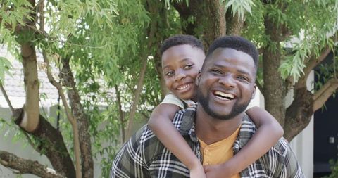 Joyful Father Carrying Smiling Son Amidst Greenery Outdoors