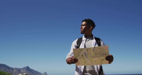 African American Hiker Holding Map Looking Toward Ocean on Coastal Mountain Trail