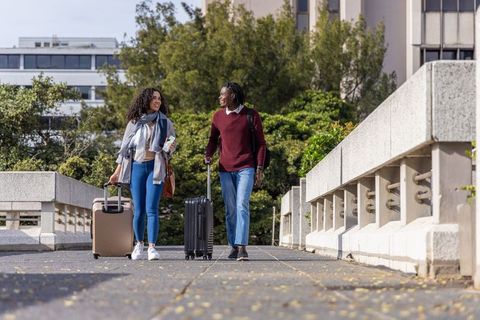 Multicultural friends walking with suitcases on urban bridge, city travel lifestyle