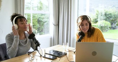 Female podcasters recording conversation in home studio with microphones and headphones