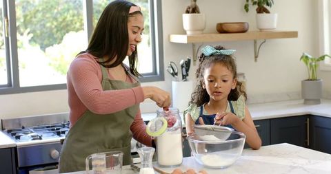 Mother and daughter baking together in bright kitchen, sifting flour for cookies
