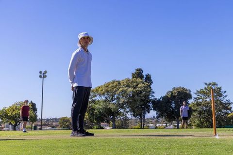 Diverse men training cricket fielding on sunny grass pitch with wooden stumps and bucket hat