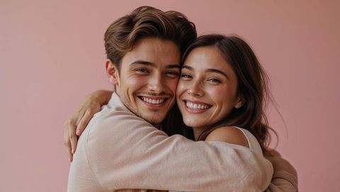Cute couple embracing cheerfully against pink backdrop