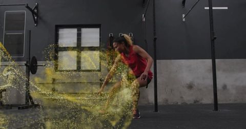 Female athlete reaching during dynamic crossfit workout with yellow motion powder trail