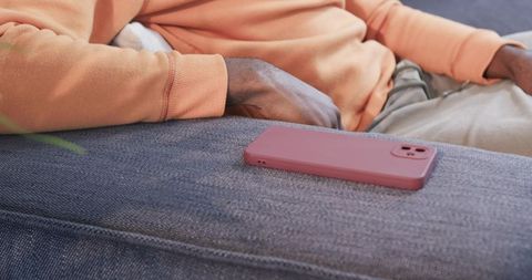 African american man reclining on blue sofa with pink phone on armrest, relaxed lifestyle