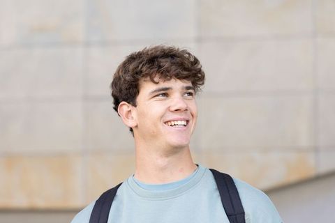 Smiling teen student wearing backpack on urban campus looking upward