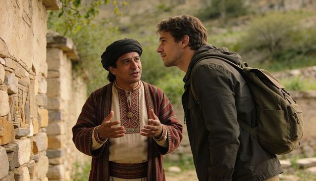 Local guide explaining stone carvings to traveler with olive green backpack